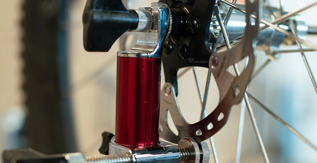 Atelier vélo avec une roue aluminium posée sur un support de centrage, outils visibles en arrière-plan flou