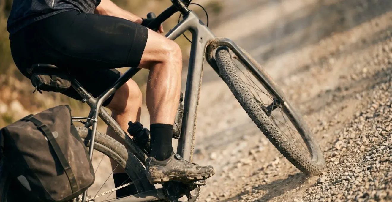 Gros plan sur les jambes d'un cycliste pédalant en montée avec un VTC chargé montrant l'effort physique